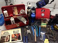 Photo showing a collection of bicycle maintenance tools, lubricants, bike chains, repair books, and water bottles with a metal toolbox.