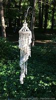 Full view of shell hanging mobile outdoors, showing length and spiral shell strands.