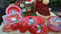 Full view of the lot showing vintage metal Christmas cookie tins with snowman and Santa designs, assorted red and white holiday serving trays, red glass heart-shaped dishes, snowman figurine, and two tinsel garland Santa hats.