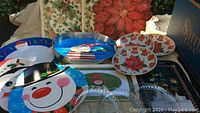 Photo of poinsettia table mats, holiday-themed serving trays including snowmen and poinsettia designs, and clear plastic cookie plates.