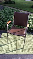 Mid Century Modern style chair shown from an angle, highlighting the wood armrests and chrome frame with light surface rust.