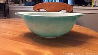 Side view of blue-green vintage Pyrex Cinderella mixing bowl with white Amish Butterprint design showing handles and pattern details.