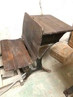 Side view of antique school desk showing cast iron legs, wooden seat, and top surface.