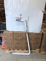 Full view of the assembled white metal bike work stand leaning against boxes.