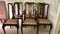Set of six wooden dining chairs, two captains with armrests, four regular side chairs, all with striped upholstered seats in peach, cream, and blue tones.