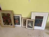 Five framed artworks arranged on floor by wall