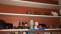 Shelf with diverse figurines including ceramic soldiers, wooden animals, brass decorative items, and a white elephant figurine.