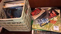 Large crate filled with vinyl records, some loose 45 RPM singles, and record sleeves including a green cover and various 33 and 45 RPM albums.
