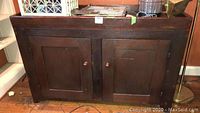 Front view of wood server/buffet with two paneled doors and round wooden knobs, dark finish, showing wear.