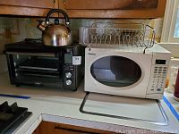 Photo of a black Bella Pro Series convection oven next to a white Chefmate microwave, with a metal teapot on top of the oven, showing overall condition and grouping of lot items.