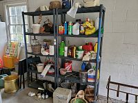 Photo showing two black plastic shelving units side by side in a garage or storage area with various household and gardening chemicals and baskets stored on the shelves.