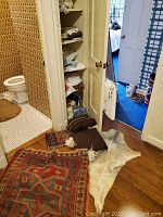 Photo showing multiple rugs on floor near bathroom door and folded linens on shelf nearby.