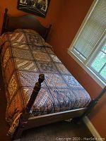 Full view of twin bed frame with patterned bedspread in room near window