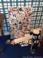 Board covered in assorted campaign buttons with box of cards and postcards at base and rolled posters to the right