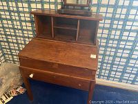 Wooden student desk showing the stain on the surface, drop-down top open to storage, and cubby storage section above.