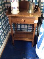 Full view of wooden side table with single drawer and objects on top, showing general condition and style.