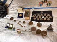 Full spread of collectible coins, medals, pins, and boxed items on white surface