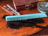 Photo showing multiple combs, decorative pens, and bowls with the leather box in the background.