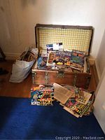 Open wooden trunk on floor filled with comic books and a bag of additional comics to the side