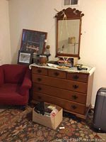 Room corner with framed wall art leaning on a dresser, a red chair, and box of books on floor