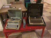 Hermes 3000 typewriter on left, Smith Corona Enterprise XT typewriter on right with gray corded phone beside them all on a small red table.