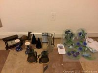 Wide view of the lot showing mantel clock, candlesticks, black conical holders, figurine, and six floral glass plates wrapped and unwrapped on floor.