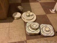 Photo showing stacked plates, saucers, cups, some bowls and glasses arranged on floor.