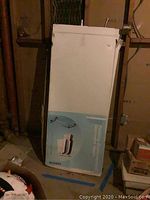 Full view of the boxed garment racks standing upright in a room with other stored items.