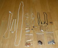 Full overview of jewelry lot items including pearl necklaces on left, silver bracelets in center, black bead necklaces and earrings on right, and assorted charms and pendants in bags below