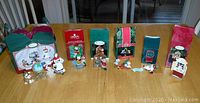 Photo showing all six Hallmark and Carleton Card Christmas ornaments with their original boxes lined up on a wooden table.