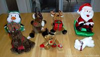 Photo of 6 Christmas stuffed animals placed on a wooden table showing different angles and all items in the lot.