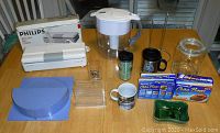 Philips vacuum bag sealer, Brita water jug, paper towel holder, Tupperware lid holder, mugs, clear glass jar on wooden table