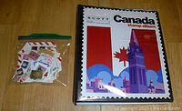 Photo showing Scott Canada stamp album next to baggie of loose stamps on a wood floor.