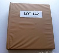 Closed brown album binder labeled Lot 142 containing first day covers.