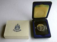 Photo showing the closed case with the coin inside and the beige outer box with Canada emblem.