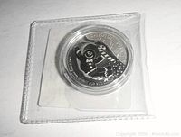 Silver coin in plastic case showing the gingerbread man on snowboard design