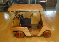 Front-left side view of the wooden golf cart showing roof, steering wheel, seats, and golf bag with wooden clubs.