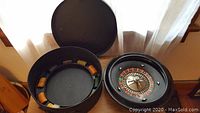Open black Bakelite travel roulette case showing wheel on right and inner chip storage on left containing poker chips.