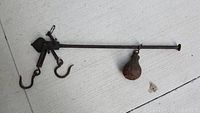 Top view of antique cast iron barn scale showing two hooks, weight on the opposite end, and mechanical adjustment elements.