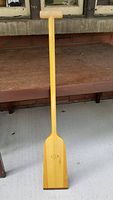 Full view of the Grey Owl 202A standard wooden racing paddle upright, showing T-shaped handle and flat blade on wooden deck
