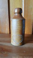 Front view of an antique brown stoneware bottle with embossed marking.