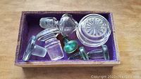 Photo of nine antique glass bottle stoppers in wooden box with purple felt lining illustrating vintage variety.