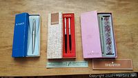 Boxed pen and mechanical pencil sets from Parker and Sheaffer in original boxes, showing three sets side by side with their respective boxes.