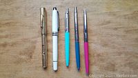 Five pens including vintage gold-filled fountain pen missing nib, white fountain pen and three ballpoint pens in turquoise, blue and pink.