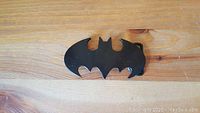 Top view of a black metal belt buckle shaped like the Batman logo, showing the smooth glossy surface.