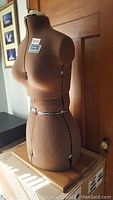 Side angled view of brown fabric-covered mannequin with adjustable measurement sections on bust, waist and hips.