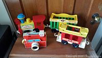 Photo of all four items: the Circus Train engine, two train cars, and the picture camera toy on a wooden surface.