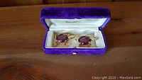 Two gold-tone turtle or tortoise brooches with purple oval stones and clear rhinestone accents in a purple velvet box with cream satin interior.