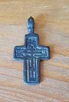 Front view of antique religious cross pendant lying flat on a wooden surface.