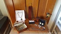Photo showing most items: Tilley leather case, chain necklaces, tie rack with brown fabric tie, cuff-links in boxes, pendants, and decorative pins arranged on a wooden surface.